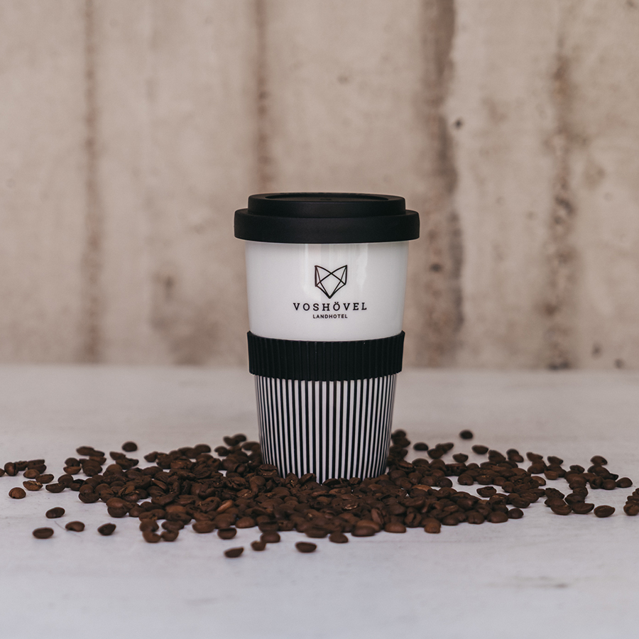 Schwarz-weißer Kaffe-to-go Becher mit dem Voshövel Logo in Kaffeebohnen