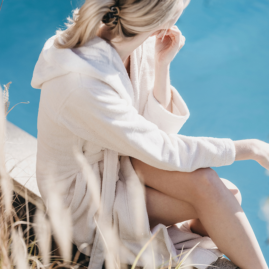 Frau sitzt im Bademantel am Pool